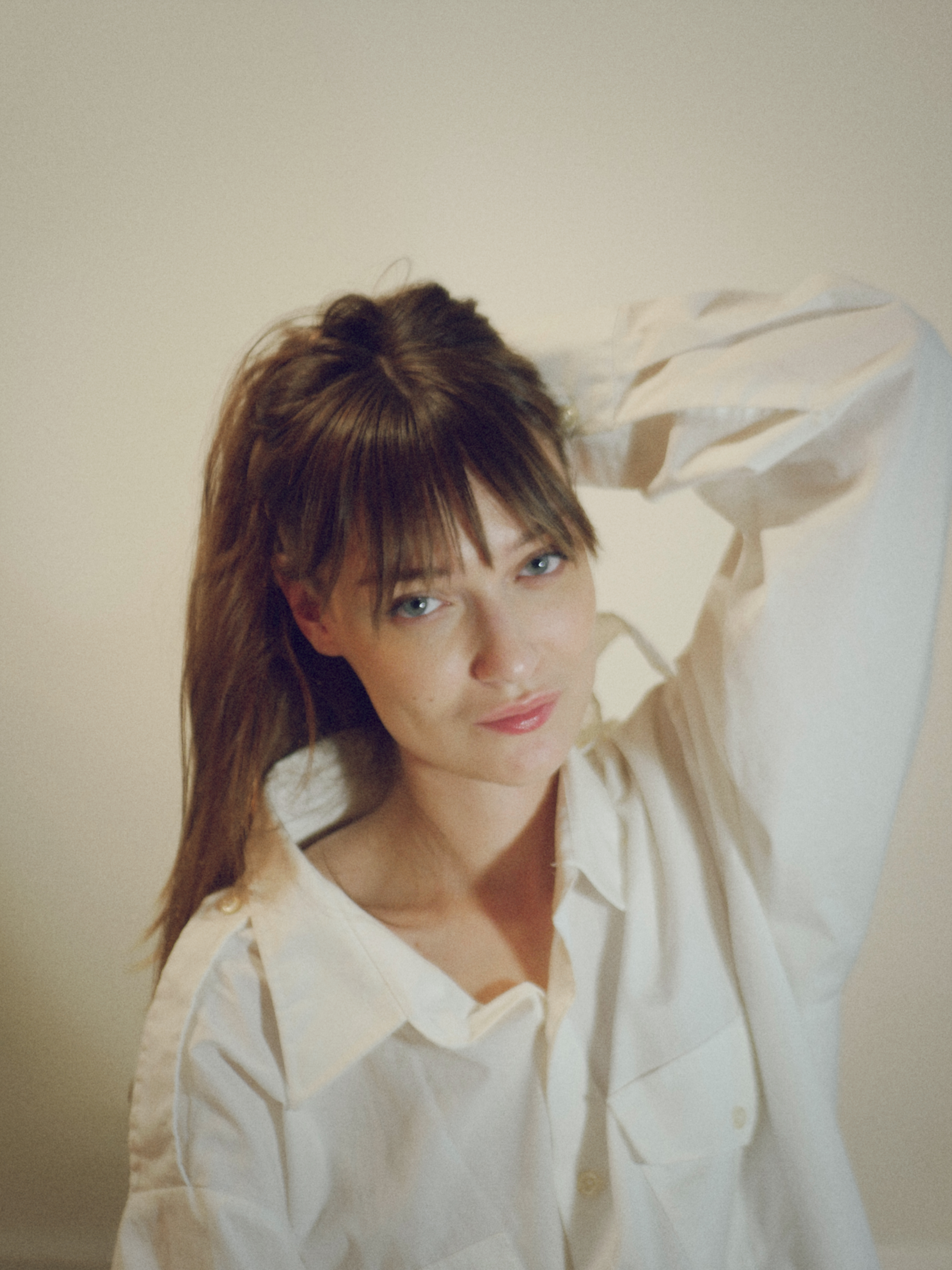 Kris Brouillette resting her head on her shoulder, looking into the camera in an oversized white shirt